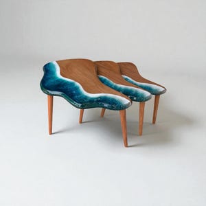 Può includere: Tre tavolini in legno dal design unico. I tavoli hanno una finitura in legno naturale sulla parte superiore, con un design a onde in tonalità di blu e bianco. Ogni tavolo ha tre gambe sottili di colore chiaro.