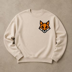 Könnte beinhalten: Cremefarbenes Sweatshirt mit einem geometrischen Fuchsmotiv in Orange, Schwarz und Weiß auf der oberen linken Brust. Das Sweatshirt hat einen Rundhalsausschnitt und lange Ärmel, ideal für Freizeitkleidung.
