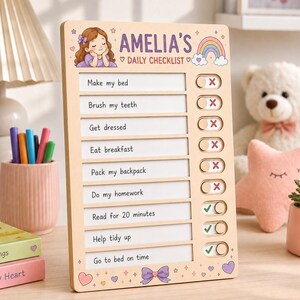 May include: A rectangular wooden daily checklist board titled AMELIA'S DAILY CHECKLIST with a cartoon girl, a rainbow, and stars. It features eight rows of tasks with sliding toggles showing red X or green check marks for tracking daily activities.