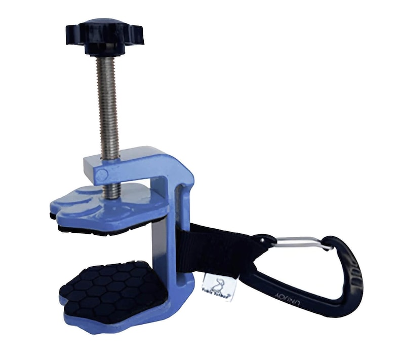 May include: A light blue clamp with a black handle and a black knob. The clamp has a screw mechanism and black pads. A black strap connects the clamp to a black carabiner clip.