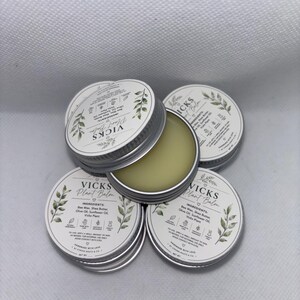 Könnte beinhalten: Eine Sammlung runder silberner Metalldosen mit Vicks Plant Balm. Die weißen Etiketten zeigen grüne Blattillustrationen, den Text Vicks Plant Balm sowie eine Zutatenliste mit Bienenwachs, Sheabutter, Olivenöl und Sonnenblumenöl.
