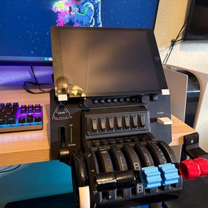Könnte beinhalten: Ein schwarzes Flugsimulator-Bedienfeld mit mehreren Hebeln, Schaltern und einem angeschlossenen Tablet. Das Panel hat blaue und rote Akzente auf den Hebeln. Der Hintergrund umfasst einen Computermonitor und eine Tastatur.