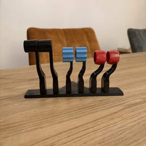 Peut inclure: Un panneau de commande noir avec quatre leviers. Les leviers ont des boutons bleus et rouges. Le panneau est sur une table en bois. L'arrière-plan comprend une chaise marron et un mur blanc.