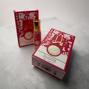 Op de afbeelding: Een roll-on parfumflesje en twee rode dozen met witte bloemmotieven en gouden accenten. De fles en de dozen bevatten het woord "Yara" in gouden letters. De dozen vermelden ook "Roll on perfume free from alcohol" en de fles bevat 10 ml.