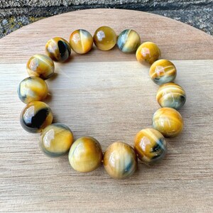 May include: A bracelet made of polished, round tiger's eye beads. The beads are primarily golden yellow with streaks of black and blue. The bracelet is displayed on a wooden surface, showcasing the natural variations in the stone.