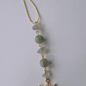 May include: A gold-toned ball chain ornament featuring a vertical arrangement of three pale blue-grey irregular stone chips and two smooth round sage green beads, terminating in a gold-toned sun charm with a central iridescent cabochon.