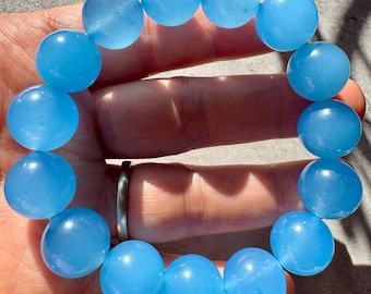 May include: A light blue beaded bracelet. The bracelet is made of large, round, translucent beads. The beads are a soft, pastel blue color. The bracelet is worn on a wrist.