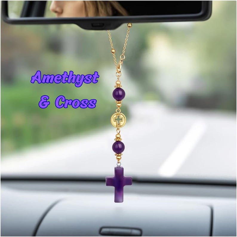 May include: A car rearview mirror hanging ornament featuring a gold-tone chain with two round purple amethyst beads, a small gold-tone circular charm with a cross cutout, and a larger purple amethyst cross pendant. The text Amethyst & Cross is visible.