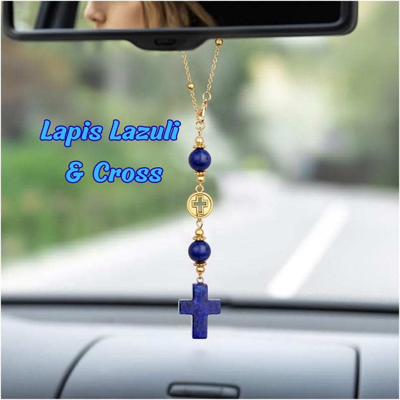 May include: A car rearview mirror hanging ornament featuring a gold-tone chain, two round deep blue lapis lazuli beads, a small gold-tone circular charm with a cross cutout, and a larger lapis lazuli cross pendant. The text Lapis Lazuli & Cross is visible.