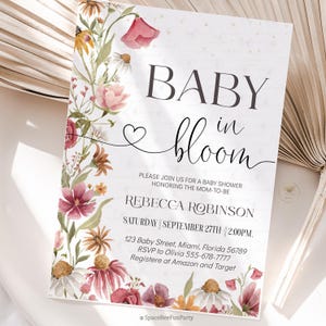 May include: Baby shower invitation with floral border. The invitation reads "BABY in bloom" with the name Rebecca Robinson, date, time, and location. The floral border includes pink, red, and yellow flowers.