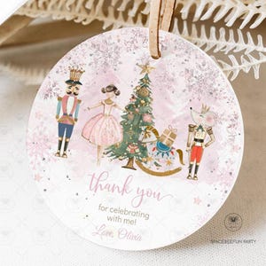 Puede incluir: Adorno navideño redondo, rosa y blanco, con temática de Cascanueces. El adorno presenta una bailarina, un árbol de Navidad y un rey ratón. El texto "Thank you for celebrating with me! Love, Olivia" está escrito en él.