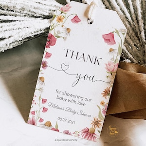 May include: A white gift tag with a floral design featuring pink and yellow flowers. The tag reads "THANK YOU" with a heart symbol and the text "for showering our baby with love." It also includes the text "Melissa's Baby Shower" and the date "08.27.2021."