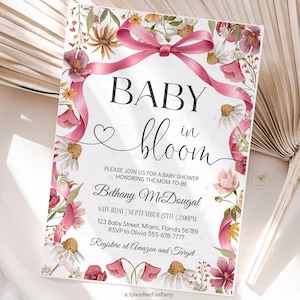 May include: Baby shower invitation with floral and ribbon design. The invitation features the words "Baby in Bloom" in elegant script, along with event details. The design includes pink and white flowers and a pink ribbon.