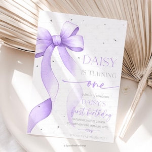 May include: A lilac birthday invitation featuring a watercolour bow and ribbons. The text reads "DAISY IS TURNING one" and includes details for the first birthday celebration. The invitation is set against a white backdrop.
