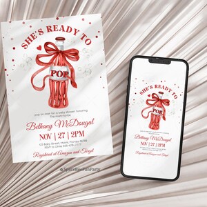 May include: A baby shower invitation and a smartphone showing the same design. The invitation features a red bottle with a bow, the word "POP", and the text "SHE'S READY TO". The invitation also includes event details.