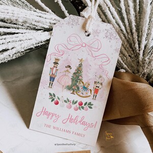 Könnte beinhalten: Ein rosa-weißes Weihnachtsgeschenkanhänger mit einer Illustration eines Weihnachtsbaums, Nussknackern und einer Ballerina. Der Anhänger trägt die Aufschrift "Happy Holidays!" und "The Williams Family."