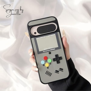 May include: A grey and black phone case designed to look like a retro handheld games console. It has a screen, directional pad, and coloured buttons. The text "GAME BOY ADVANCE SP" is visible.