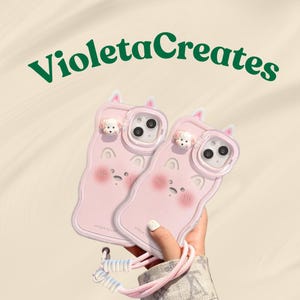 May include: Two pink phone cases with a cartoon dog design, featuring a strap. The cases have a cute face design with blush and a small dog on top. The text "VioletaCreates" is in green cursive.
