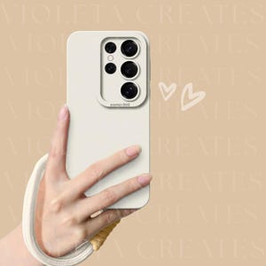 Puede incluir: Funda de teléfono de color crema con protector de lente de cámara y correa para la muñeca. La funda tiene un acabado liso y forma rectangular. El protector de lente tiene un borde elevado. La correa es crema y amarilla.