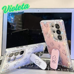 Könnte beinhalten: Transparente Handyhüllen mit Blumenmustern und Strassakzenten. Ein pinkfarbener Pop-Socket und ein weißer Pop-Socket mit Blumengrafiken sind ebenfalls zu sehen. Der Text "Violeta Creates" ist sichtbar.