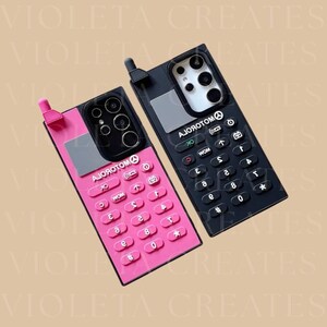 May include: Two phone cases in a retro design. One is pink with a black camera and keypad, the other is black with a white camera and keypad. Both cases have a keypad with numbers and symbols. The text "AJОЯОТОМ" is visible on both cases.