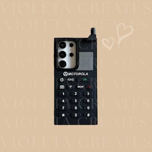 May include: A black phone case with a retro Motorola design. The case features a keypad with numbers and symbols, a camera cutout, and the Motorola logo. The design includes an antenna and a small screen area.
