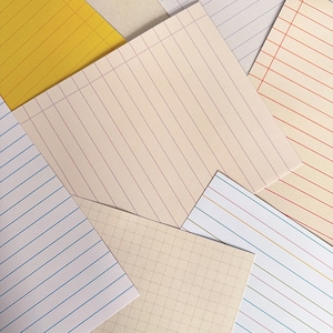 Può includere: Una collezione di fogli di carta da lettere con vari motivi, tra cui linee orizzontali gialle, blu e rosse, oltre a un motivo a griglia beige. I fogli sono sovrapposti, mostrando diversi colori e spaziature tra le linee.