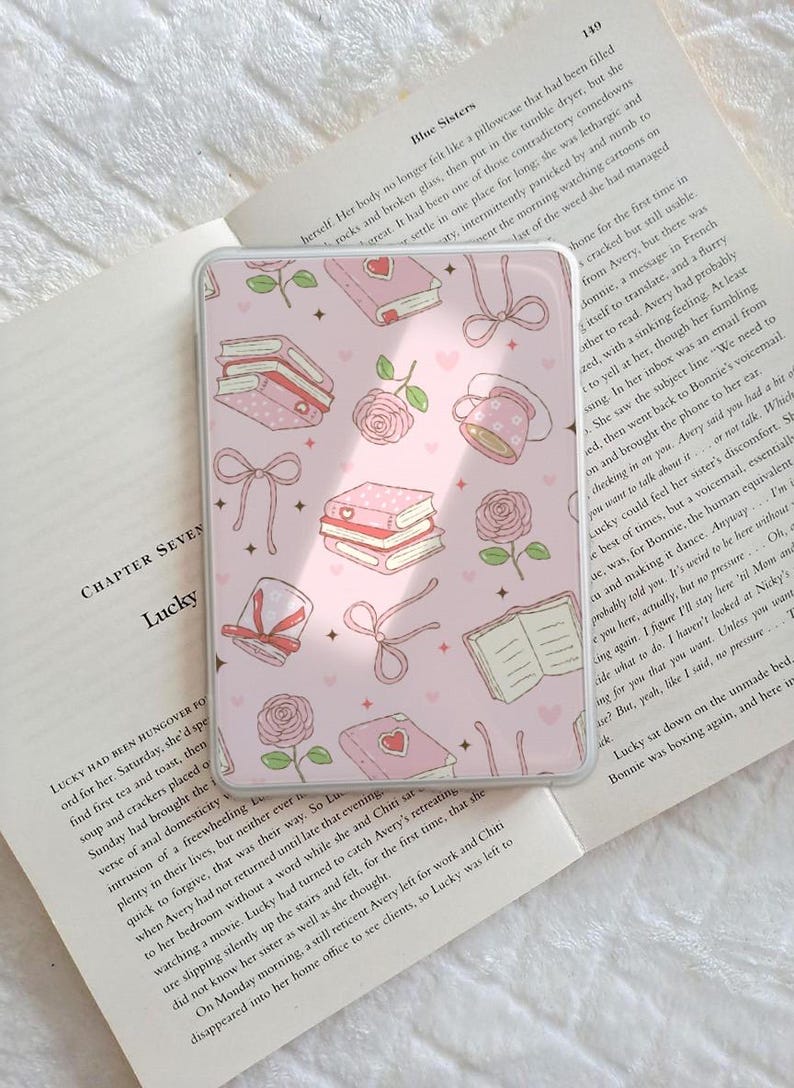May include: A pink phone case with a repeating pattern of books, roses, bows, and teacups. The design has a soft, feminine aesthetic, perfect for a book lover or someone who enjoys floral motifs.