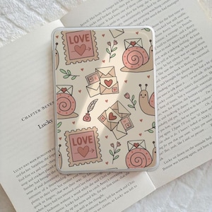 May include: A phone case with a repeating pattern of pink postage stamps with hearts, envelopes, snails, and sprigs on a cream background. The stamps read "LOVE".
