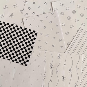 May include: An assortment of white paper sheets featuring diverse black patterns. Designs include a chequered pattern, stripes, hearts, stars, bows, flowers, and smiley faces. The sheets are arranged in an overlapping layout.