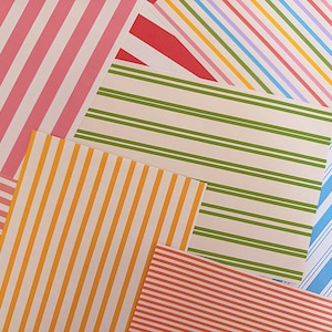 Può includere: Una collezione di fogli di carta rettangolari caratterizzati da vari motivi a righe in colori vivaci tra cui rosa, rosso, giallo, verde e blu. Le righe variano in larghezza e orientamento sui diversi fogli, creando una disposizione a strati.