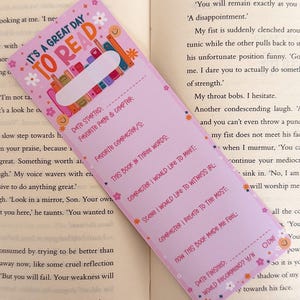 May include: A rectangular light purple reading tracker bookmark featuring the text IT'S A GREAT DAY TO READ, a row of colorful books, and prompts including Date Started, Favorite Character, This Book in Three Words, and Date Finished.