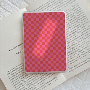 Peut inclure: Une coque de téléphone à carreaux roses et rouges. L'étui présente un motif vibrant de carrés alternés en deux nuances de rose et de rouge. L'étui rectangulaire semble être fait d'un matériau lisse.