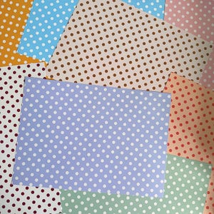 Könnte beinhalten: Eine Sammlung überlappender rechteckiger Papierbögen mit verschiedenen Punktmustern. Die Farben umfassen Senfgelb, Hellblau, Braun, Rosa, Dunkelrot, Lavendel, Orange und Minzgrün, alle mit weißen kreisförmigen Punkten versehen.