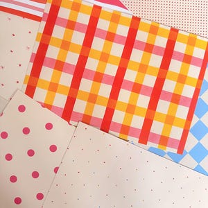 May include: A collection of patterned papers featuring various designs including a bright red, orange, and yellow plaid, large pink polka dots on cream, small multicolored dots, a red and white striped sheet, and a light blue and white checkered pattern.