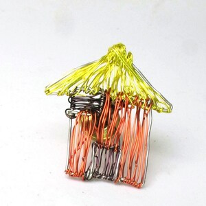 May include: A small wire sculpture of a house with a yellow roof and orange and silver walls.