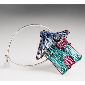 May include: A silver bangle bracelet with a blue, teal and pink wire sculpture attached. The sculpture is shaped like a house.