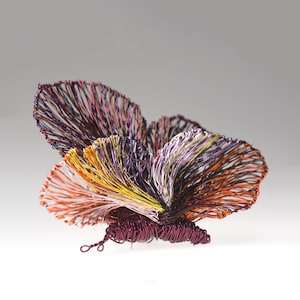 May include: A wire sculpture of a butterfly. The wings are made of colourful wires in shades of orange, purple, yellow, and red. The body is a deep burgundy colour. The sculpture is a decorative art piece, suitable for display.