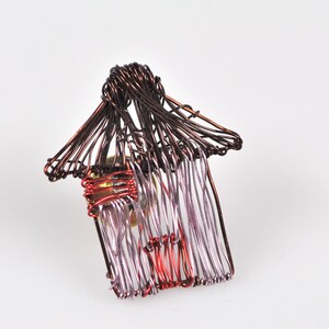 May include: A wire sculpture of a house with a red and purple roof and a brown base.