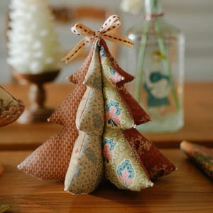 May include: A handmade fabric Christmas tree with a bow on top. The tree is made of various patterned fabrics in shades of brown, green, and red. The tree is approximately 6 inches tall and is a decorative item.