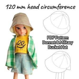 Op de afbeelding: Een pop draagt een beige vissershoed, een gele top met een afbeelding, een groen geruit overhemd en een spijkerbroekshort. De tekst "120 mm hoofdomtrek" staat boven de pop. De afbeelding bevat ook tekeningen van een muts en een vissershoed.