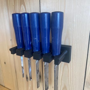 May include: A set of five wood chisels with blue handles and silver blades, mounted on a black holder. The chisels are arranged in a row, showcasing their sharp edges. The tools are designed for woodworking.