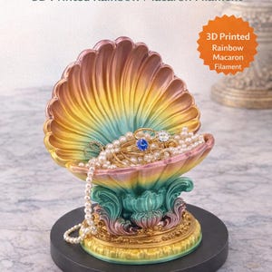 May include: A 3D-printed seashell jewelry holder in rainbow colors, filled with jewelry and pearls. The base is black, and the text "Stunning Sea Shell Jewelry Holder" and "Shop Now Etsy" are visible.