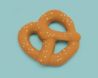 May include: A brown pretzel-shaped object with white speckles, set against a light blue background. The pretzel has a textured surface and a classic knot design, resembling a baked treat.