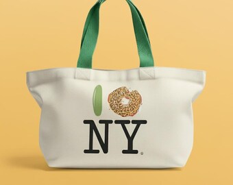 May include: Off-white tote bag with green handles. The bag features the phrase "I ❤️ NY" with a green pickle replacing the heart and a bagel replacing the heart symbol. The bag is made of a sturdy material.