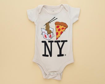 May include: A cream-colored short-sleeve baby bodysuit featuring a graphic print of a white takeout container with noodles, a slice of pepperoni pizza, and the bold black text NY. The garment has a round neckline and snap closures at the bottom.