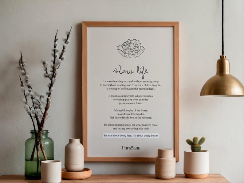 May include: A framed print with the words "slow life" in a minimalist style. The print is in a light wood frame and is displayed with decorative vases, a small cactus, and a brass pendant light.