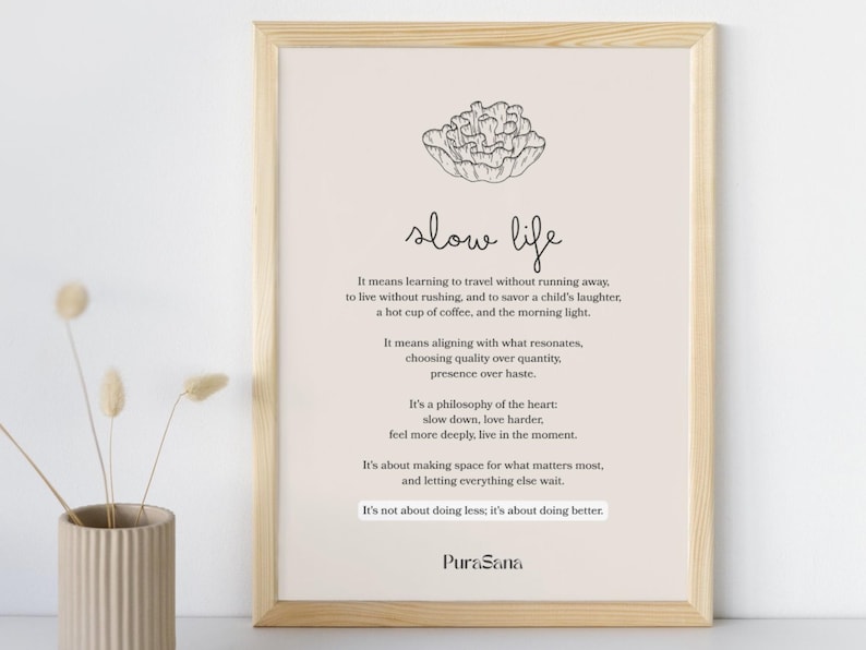 May include: A framed print with the words "slow life" in a handwritten style. The print has a beige background with black text and a line drawing of a flower. A vase with dried flowers is in the foreground.