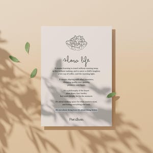May include: A beige print with the words "slow life" in cursive, accompanied by a floral illustration. The text describes a philosophy of slowing down and appreciating life's simple pleasures. Green leaves and shadows add a natural touch.