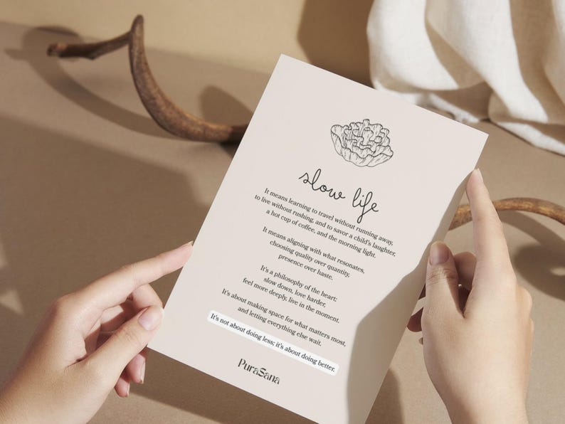 May include: A beige card with the words "slow life" in script, a floral illustration, and text about slowing down. The card is held by two hands, with a brown antler and fabric in the background.